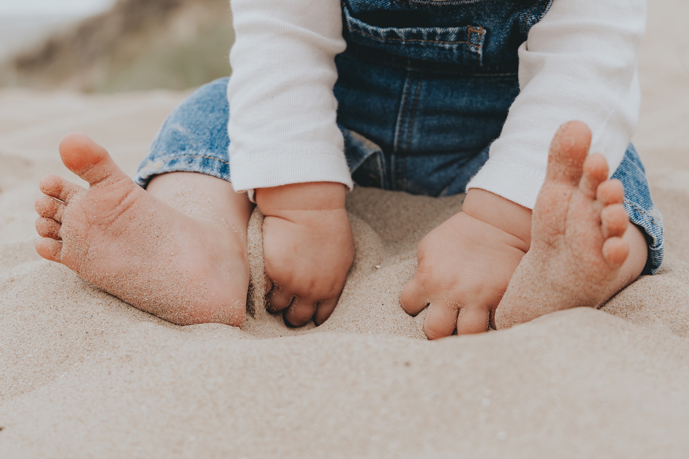 Pieds de bébé et mains d’enfant dans le sable — séance photo de famille